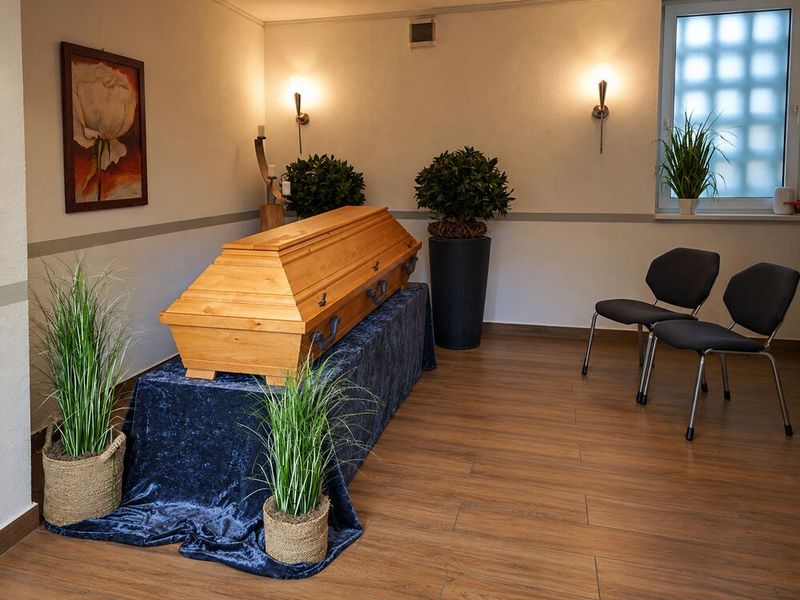 Abschiedsraum mit aufgebahrtem Holzsarg, Pflanzen und Stühlen für Angehörige